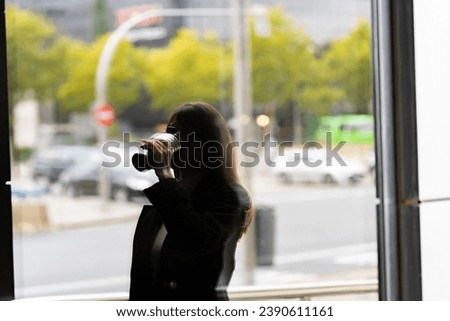 Backlit cityscape: girl with coffee, reflections in building glass, autumnal urban ambiance.