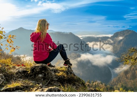 woman sitting on top of a mountain, below the clouds in a river valley