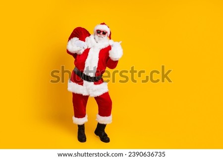 Full size portrait of eccentric santa carry christmas presents sack indicate finger empty space isolated on yellow color background