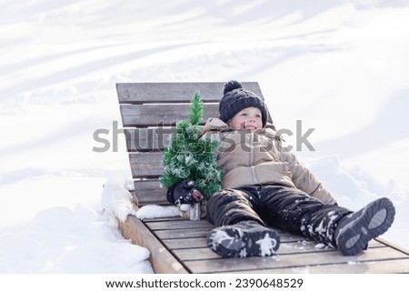 Waiting for summer. Cute little boy lying on a sunbed near Christmas tree in winter and dreaming of summer. Child runs in the winter towards the summer. concept of waiting warm. goodbye winter