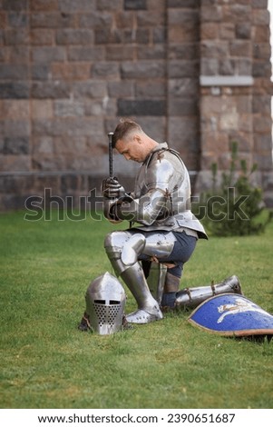 Make fealty. Portrait of serious manm medieval warrior, knight in armor sitting on one knee. Knight's noble oath. Comparison of eras, history, renaissance style