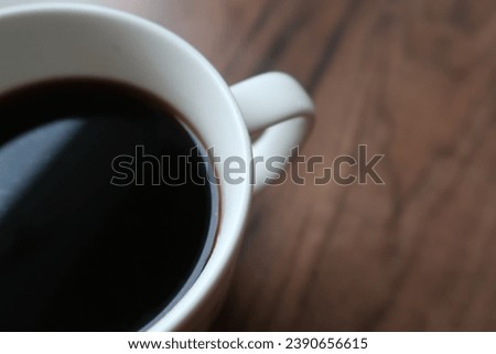 White cup of black coffee on a wooden table surface. Natural light. No people. Morning coffee, soft light. Picture taken from above.