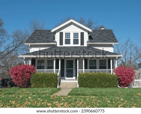 White house with large single dormer and open porch with railing and fall red bushes. Royalty-Free Stock Photo #2390660775