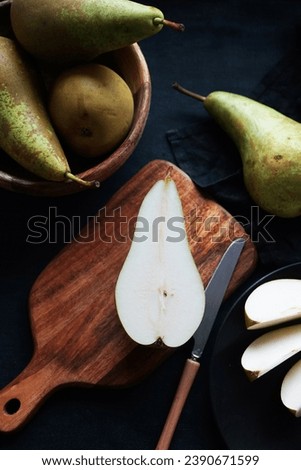 Whole and sliced ​​ripe pears on a wooden board and plates on a dark background Royalty-Free Stock Photo #2390671599