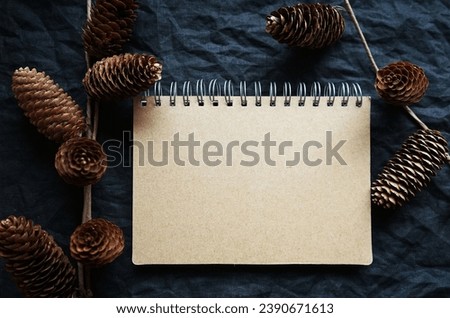 Notepad next to branches and pine cones on a dark background