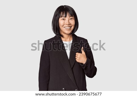 Young Chinese woman in business attire in studio smiling and raising thumb up