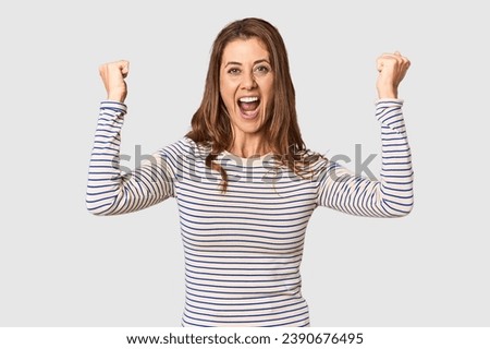 Middle-aged woman portrait in studio setting cheering carefree and excited. Victory concept.