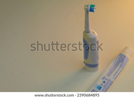 A photo of a tall, white electric toothbrush beside a squeezed tube of toothpaste.