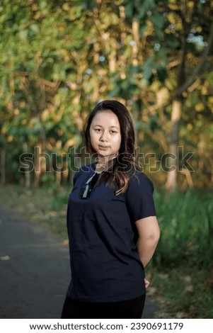 Clothing model. Young Asian woman with sunglasses posing outdoors. Asian woman wearing a plain Navy Blue t-shirt on a background of trees. It was as if he was modeling a plain t-shirt.
