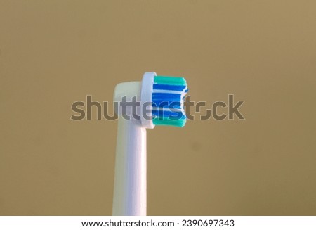 A close up photo of the green, white and blue head of an electric toothbrush against a mustard background. 
