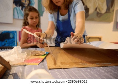 Details on white cardboard paper sheet on the desk against blurred background of a paint teacher and her little student drawing working in creative art workshop. Kids, creativity and education concept