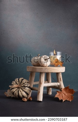 Small decorative pumpkins and aroma candle on wooden stool as cozy autumn home decor