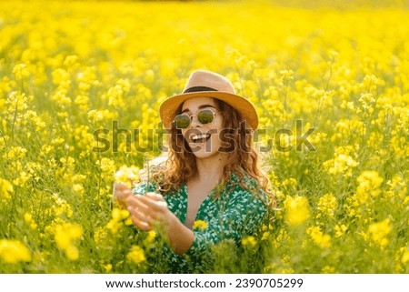 Young woman walking through a flowering field gently touches yellow flowers. A tourist in a straw hat enjoys sunny weather in a rapeseed flowering field. Nature concept.
