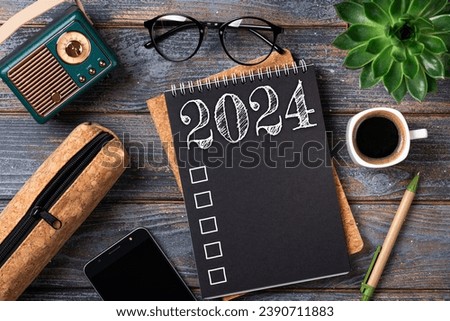 New year resolutions 2024 on desk. 2024 goals list with notebook, coffee cup, plant on wooden table. Resolutions, plan, goals, action, checklist, idea concept. New Year 2024 resolutions. Copy space Royalty-Free Stock Photo #2390711883