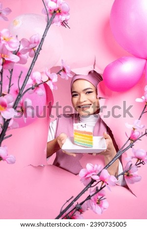 A cheerful Asian young lady wearing hijab with an empty white placard board for copyspace on pink background.
