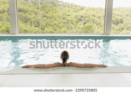 Woman swimming in a wellness center spa pool at a luxury hotel with large windows and a view of the mountains