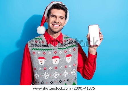 Photo of intelligent positive guy wear christmas hat demonstrate smartphone display qr code empty space isolated on blue color background