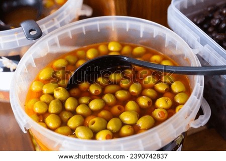 In shop window is bucket filled with salted pickled olives, stuffed shrimp, paprika. Ladle in barrel with pickled olives for convenience of supermarket customers