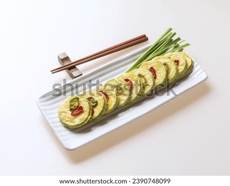 Close up of young pumpkin rice cakes in a row with raw chives leaf on square dish with wooden chopsticks on pedestal, South Korea
