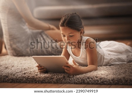 Lots to learn about the world wide web. Shot of an adorable little girl using a digital tablet on the floor at home with her mother in the background.