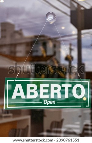 Bilingual sign with the words Aberto and Open in Portuguese and English on the glass door of a store in Brazil