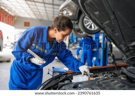 Mechanic working under the hood at the repair garage. Portrait of a happy mechanic woman working on a car in an auto repair shop. Female mechanic working on car. Female Auto Mechanic.