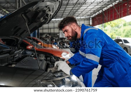 Mechanic working under the hood at the repair garage. Portrait of a happy mechanic man working on a car in an auto repair shop. Male mechanic working on car.