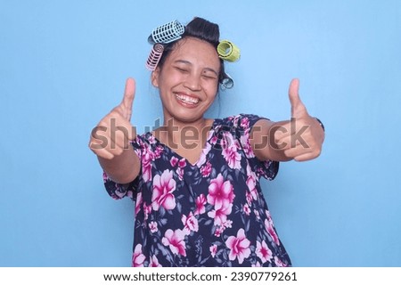 Cheerful Asian woman wear colorful hair rollers giving two thumbs up with happy expression