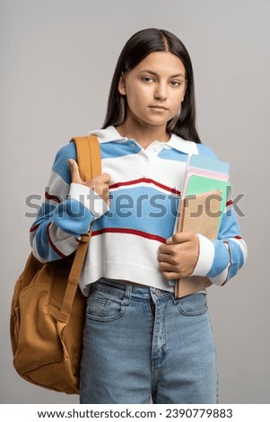 Teenage girl with backpack and notebooks. Serious unsmiling girl in confident pose looking at camera. Ready for hard studying in university college, teenager isolated on gray, studio portrait. Royalty-Free Stock Photo #2390779883