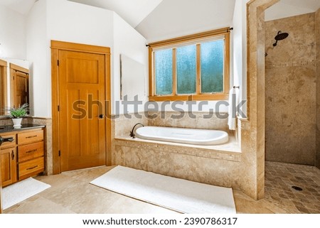 bathroom interior in white with large bathtub travertine tile glass shower white marble countertop window orchid and mirrors Royalty-Free Stock Photo #2390786317