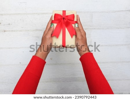 
view from above of
girl asian hands in red sweater holding craft paper gift box with red ribbon bow on a white wooden table.
for giving in special day,Christmas, new year,
Valentine