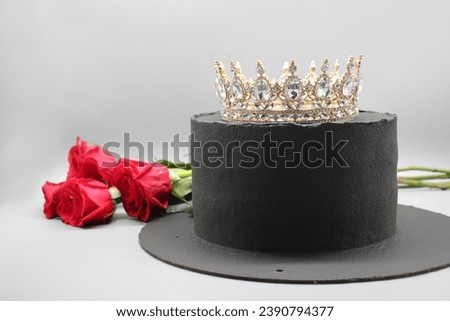 Handmade black cake with a crown on a gray background with red roses close-up.