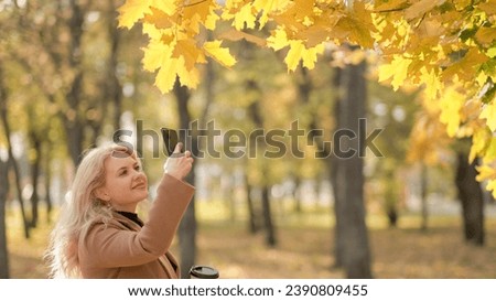 Autumn beauty. Happy woman. Mobile photo. Smiling lady staying in park shooting yellow maple tree leaves on smartphone.