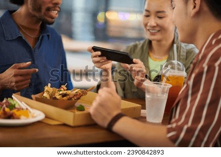 Young woman taking picture of street food when having lunch with friends