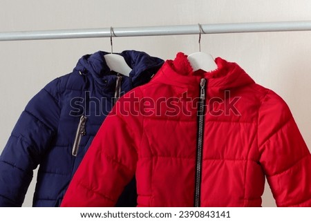 Red and blue child down jackets hanging over white background Royalty-Free Stock Photo #2390843141