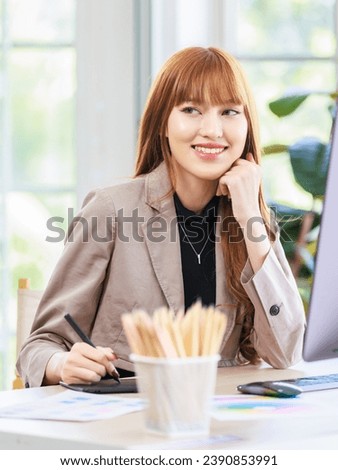 Asian professional successful young female businesswoman creative graphic designer in casual fashionable suit outfit sitting smiling working drawing sketching with stylus pen and computer in office.