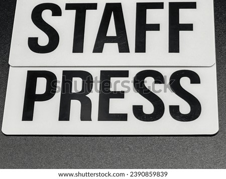 Press, staff . Black letters. On white hard plastic and dark paper background. Words. Monochrome.