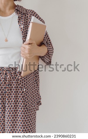 Laptop computer and paper documents in female hand. Young pretty woman in pajamas stays over white wall. Businesswoman, work at home concept Royalty-Free Stock Photo #2390860231