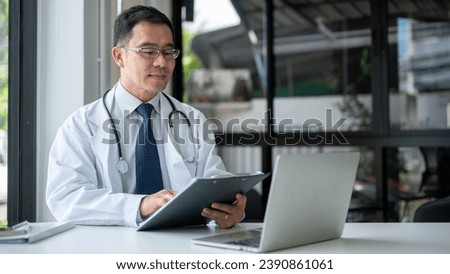 An experienced Asian senior male doctor in a white gown is examining medical cases on report at his desk in the office, working in a hospital. Health care and career concepts Royalty-Free Stock Photo #2390861061