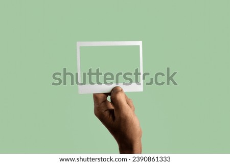 black male hand holding photo frame on isolated on light green background