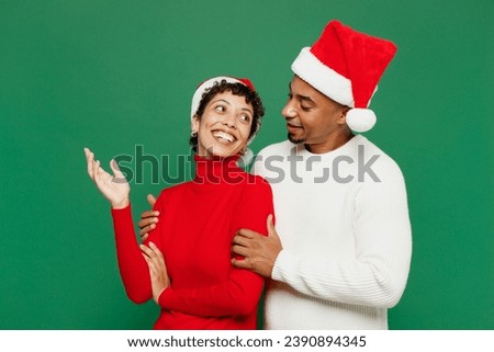 Side view merry fun young couple friends man woman wears red casual clothes Santa hat posing hug talk speak hugging isolated on plain green background. Happy New Year 2024 Christmas holiday concept