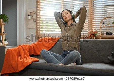 Happy young woman listening favorite music in headphone relaxing on couch at home
