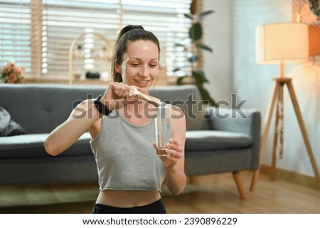 Sporty woman preparing healthy supplement, dissolving collagen powder in a glass of water