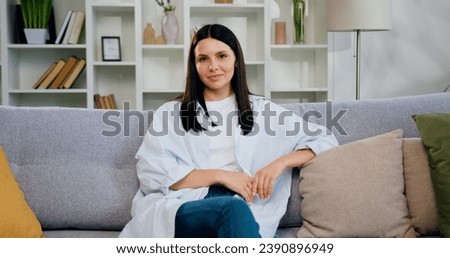 Close-up. Portrait petty house wife relax on comfort sofa smile staring at camera look happy. Happy woman sitting on sofa at home and looking at camera. Royalty-Free Stock Photo #2390896949
