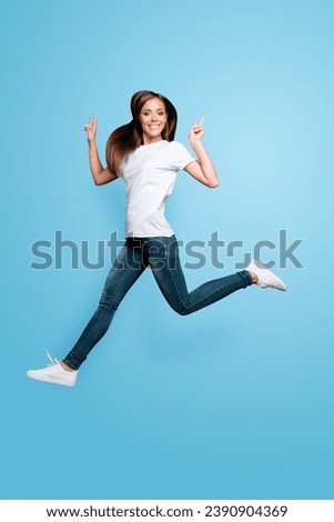 Full-body full-size portrait of cheerful girl who jumps and shows v-sign isolated on gray background