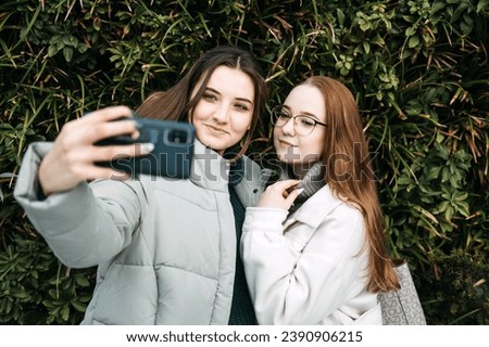 Gen Z influence on the development and popularity of short-form video content on social media platforms. Two girl friends share a moment over smartphone and record video outdoors