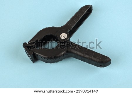 Universal plastic clip with a black spring for holding and fixing various objects and materials.