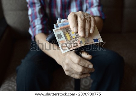 The hands of an old man holding money, euros. Close-up. Poverty, low incomes, austerity in old age, social problems. Royalty-Free Stock Photo #2390930775