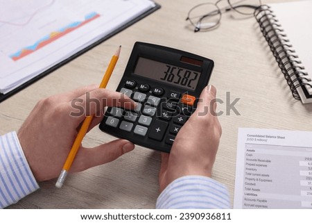 Man using calculator at wooden table, closeup