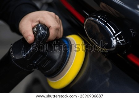 A mechanic polishes the surface of a car trunk door with a grinding machine. Royalty-Free Stock Photo #2390936887